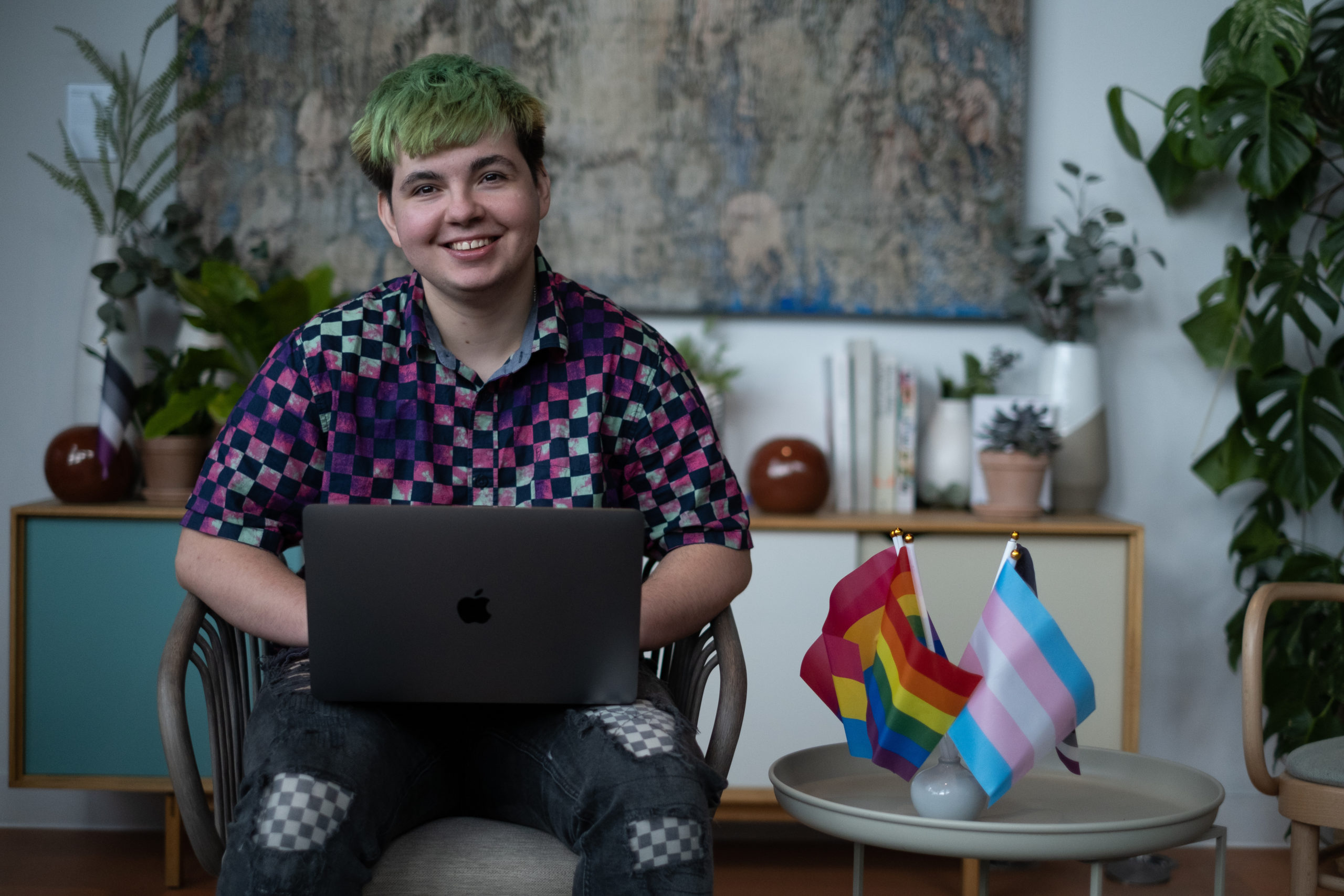 A Just Like Us volunteer sat with a laptop next to several LGBT+ Pride flags