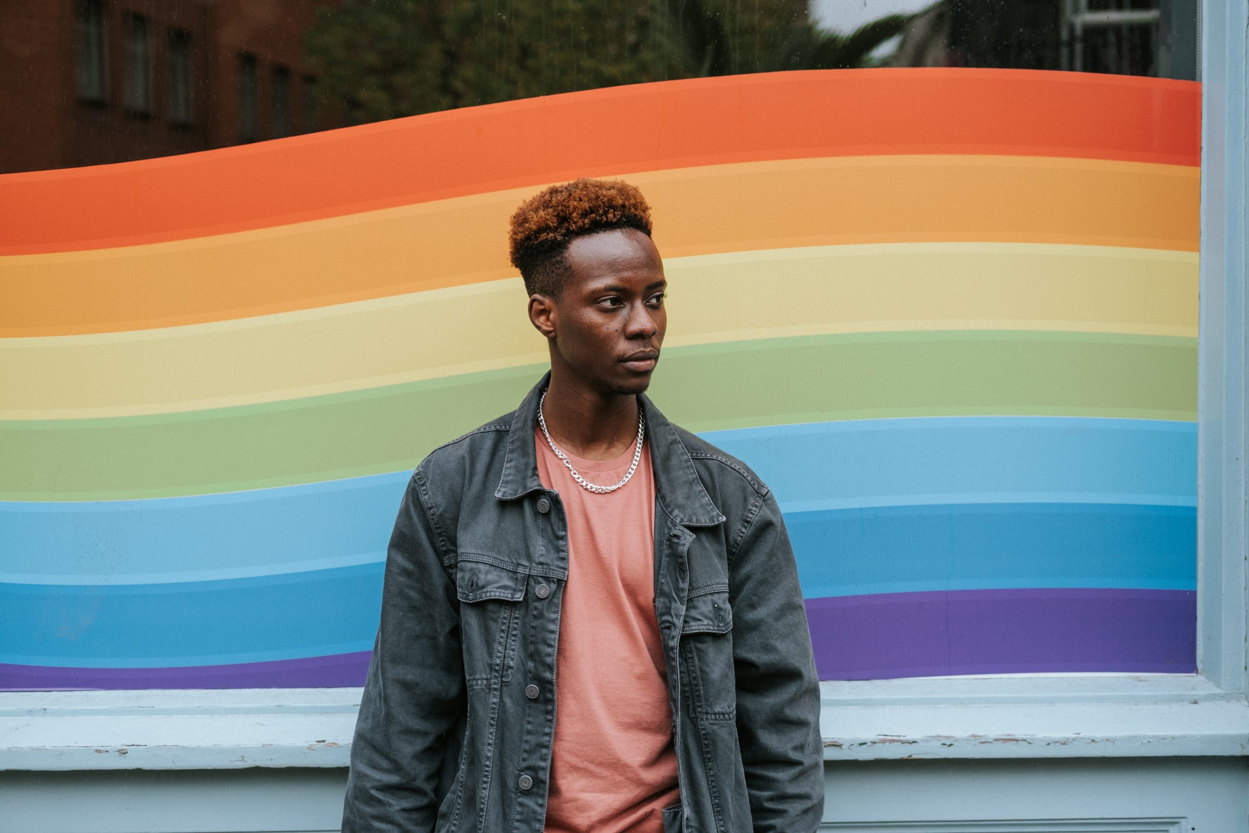A young Black man stood in front of a rainbow window display