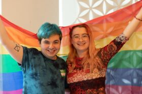 Two LGBT+ ambassadors hold a Pride flag while volunteering for Just Like Us
