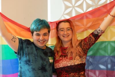 Two LGBT+ ambassadors hold a Pride flag while volunteering for Just Like Us