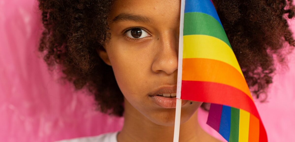 A young woman hides her face behind a rainbow Pride flag