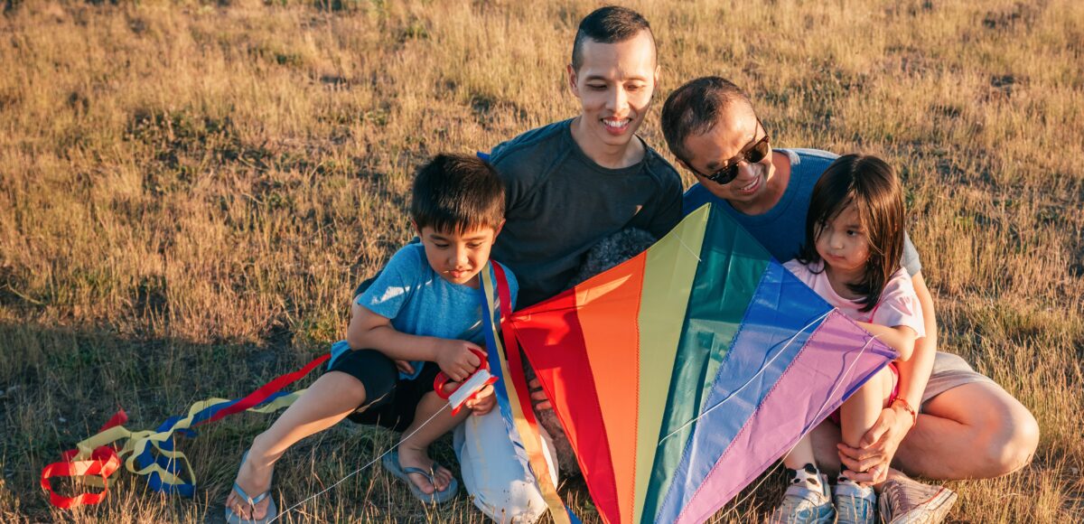 An LGBT+ family - two parents and two children - hold a rainbow kite