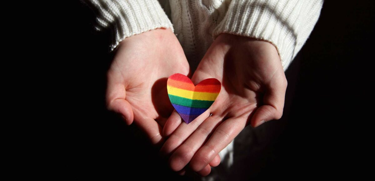 A pair of hands hold a paper rainbow heart