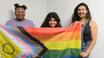 Three Just Like Us ambassadors hold up a Progress Pride flag